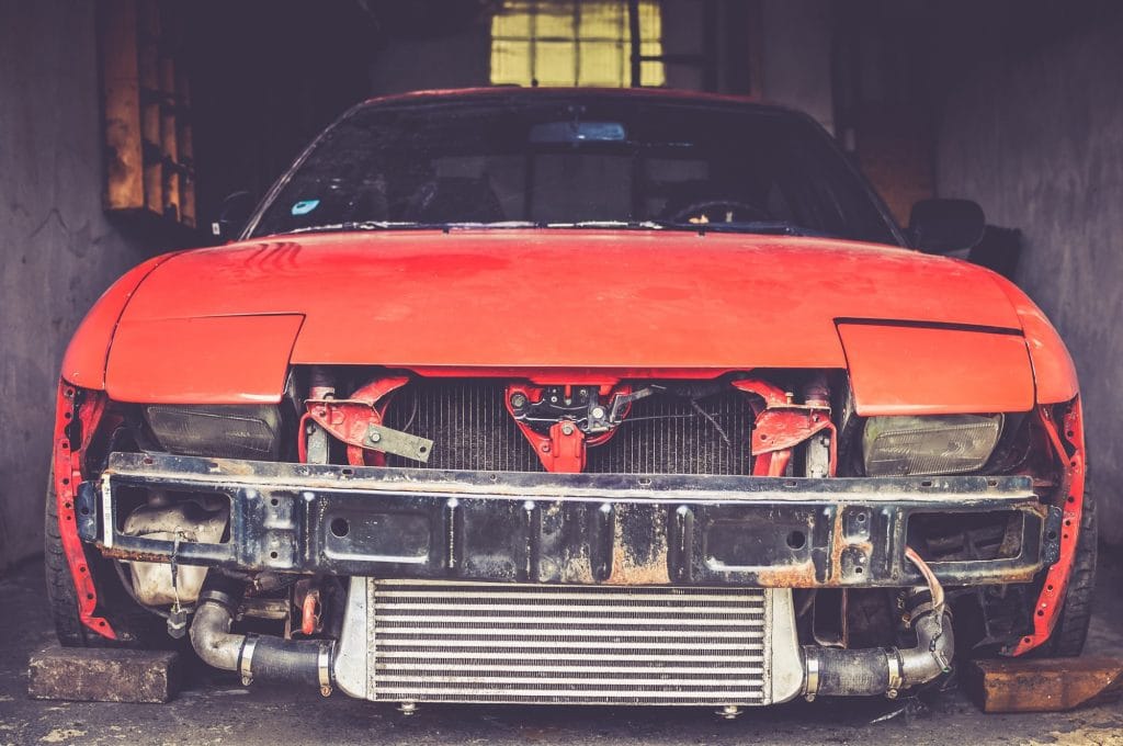 Red car missing front bumper in garage