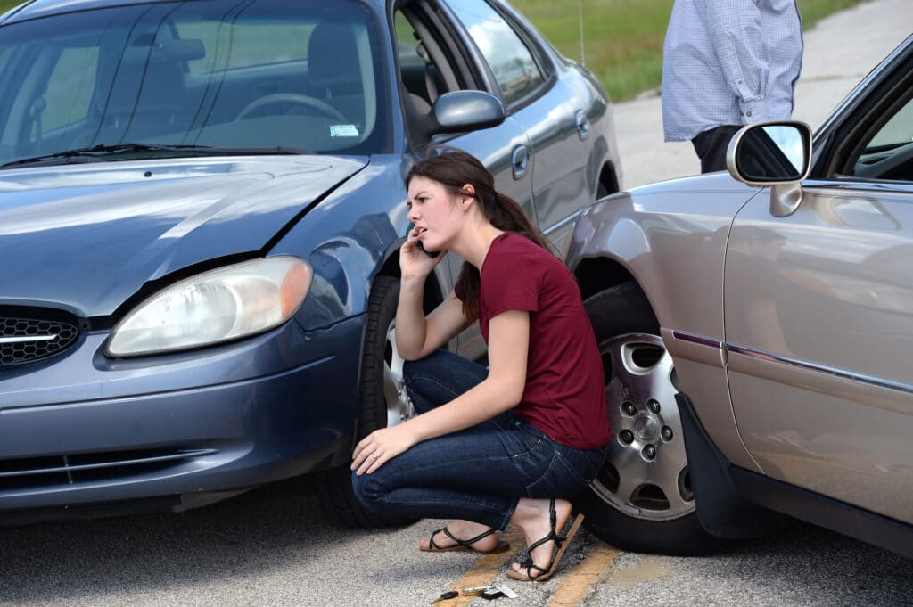 Woman on phone after car accident on road.