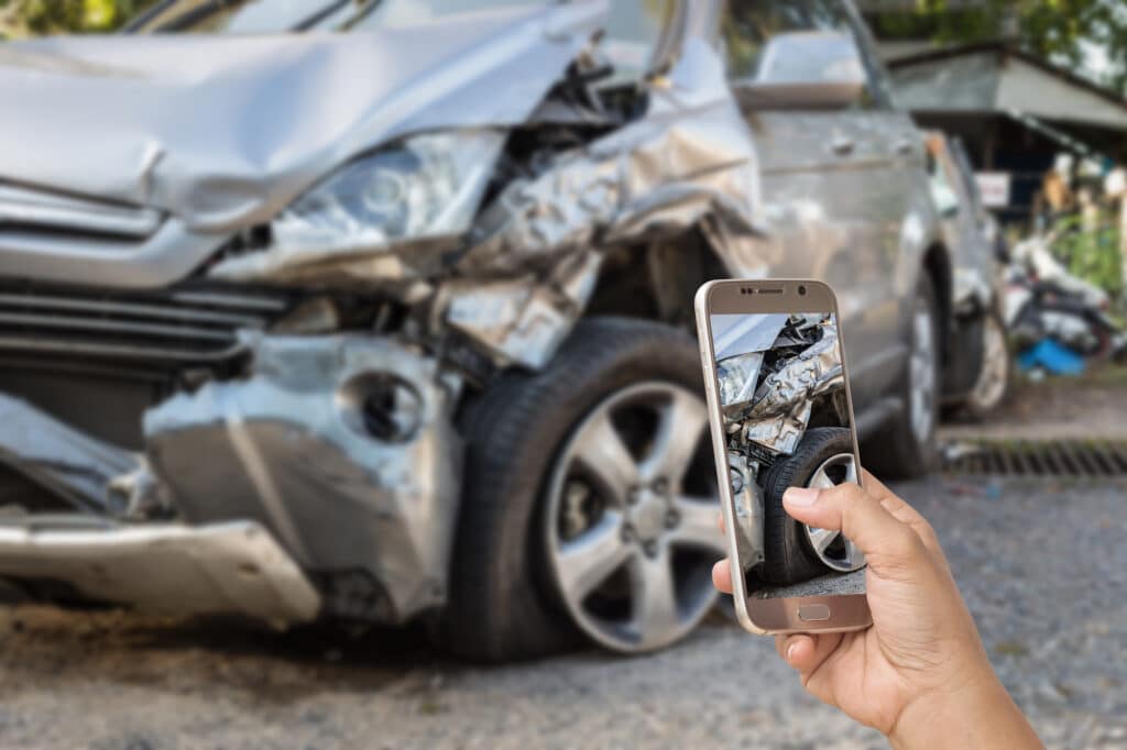 Person photographing damaged car with smartphone.