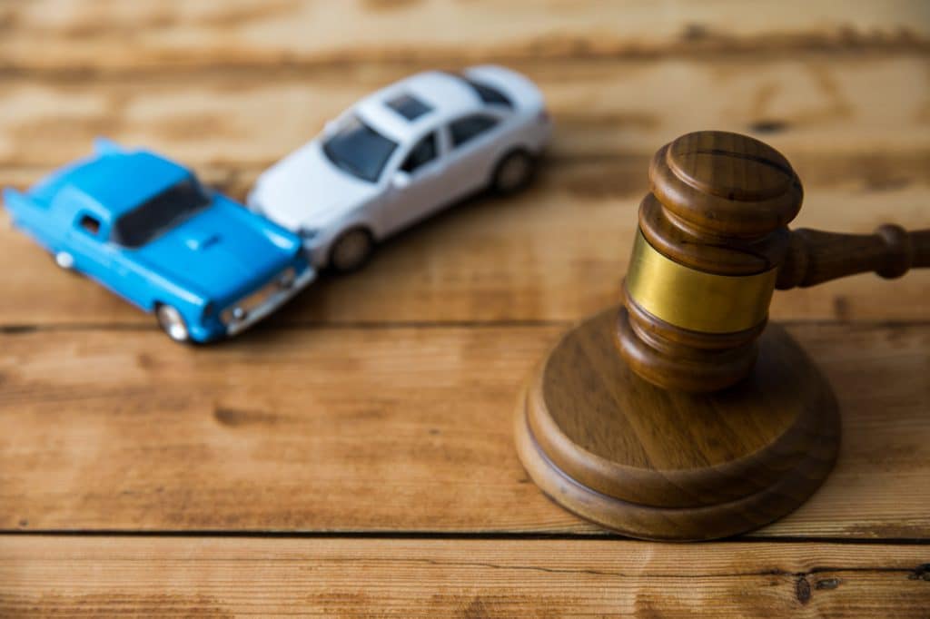 Toy cars crash beside judge's gavel on table.