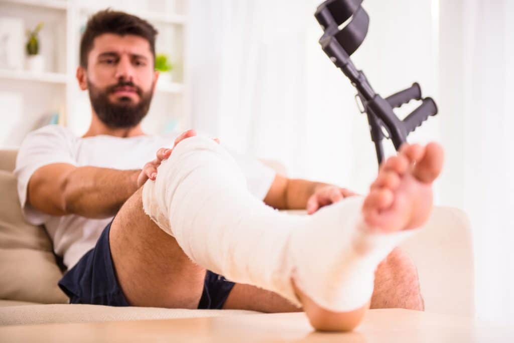 Man with leg cast resting on couch with crutches.